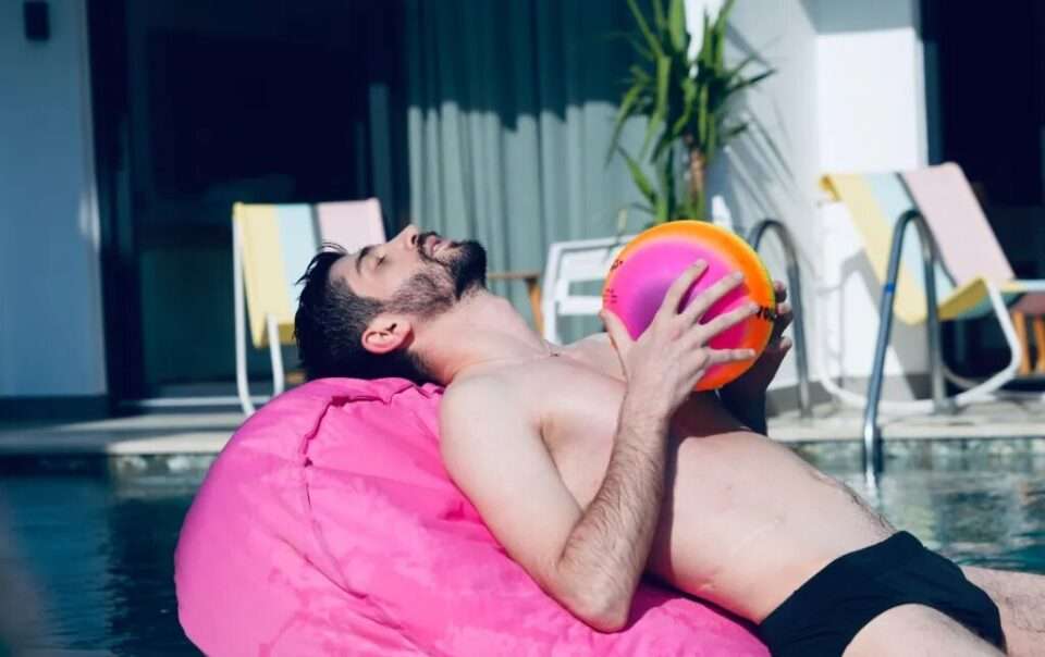 Scape Hotel - boy paying on a fluffy chair by the pool holding a ball